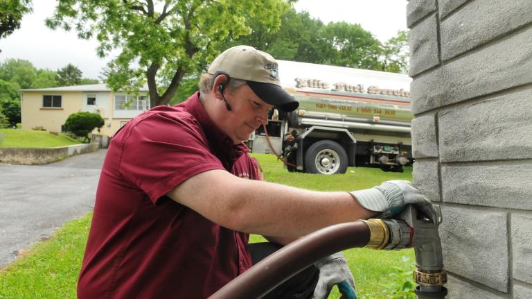 A man fills a home heating oil tank with a long hose connected to a tanker truck.