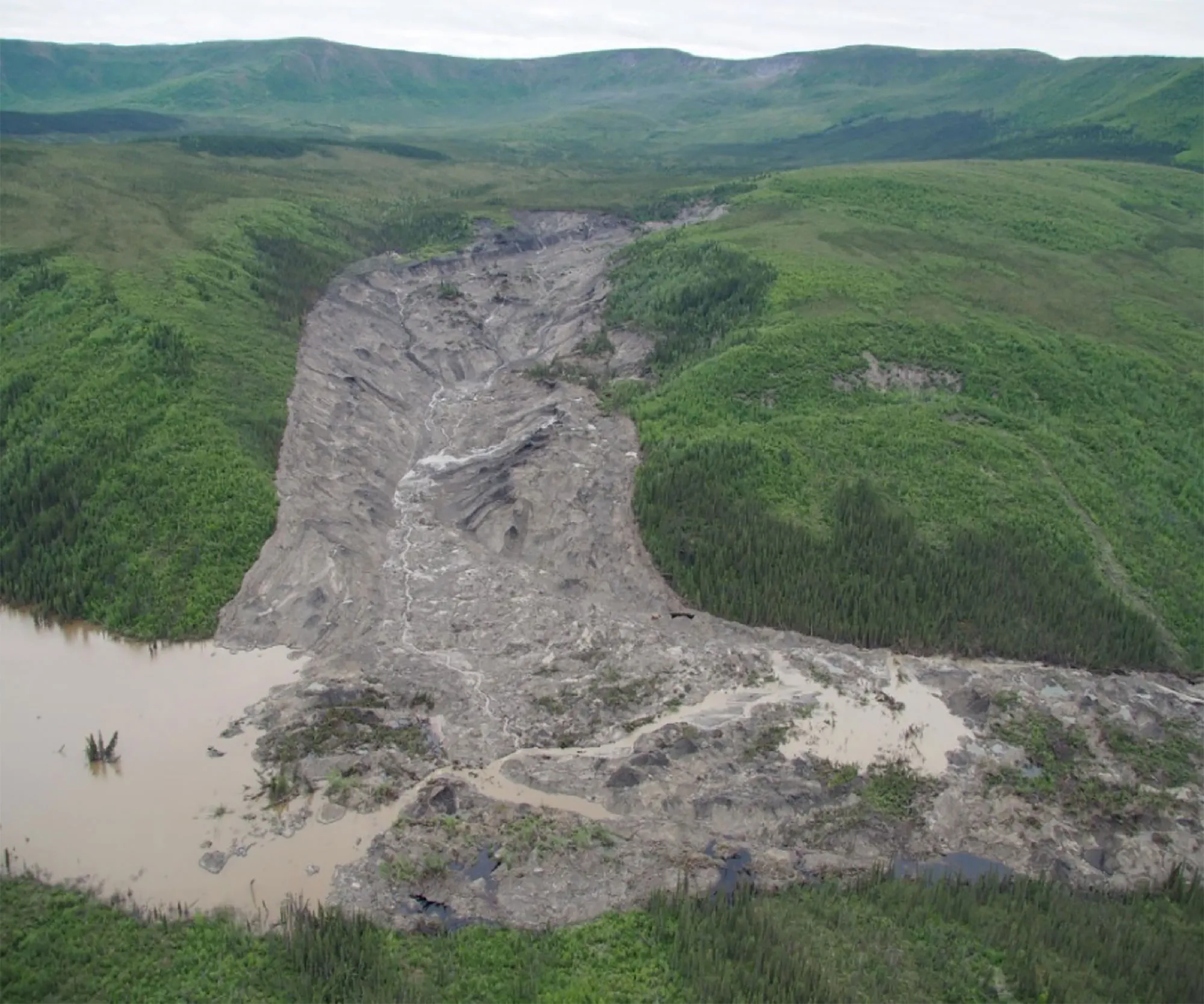 landscape showing damaged earth caused by permafrost detachment slides with tree covered hills on either side