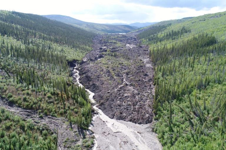 landscape showing damaged earth caused by permafrost detachment slides with tree covered hills on either side