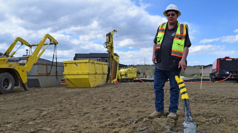 A man in a hard hat and fluorescent vest stands at a construction site